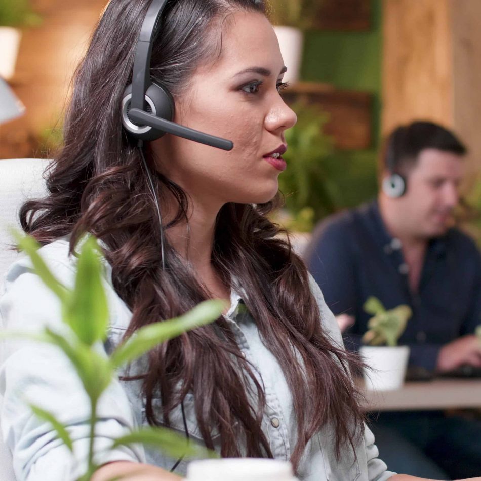 Young support customer woman talking into headset microphone with call center customer while working in startup company office. Caucasian female consultant providing telemarketing service